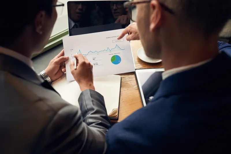 Dois profissionais analisando gráficos impressos sobre uma mesa
